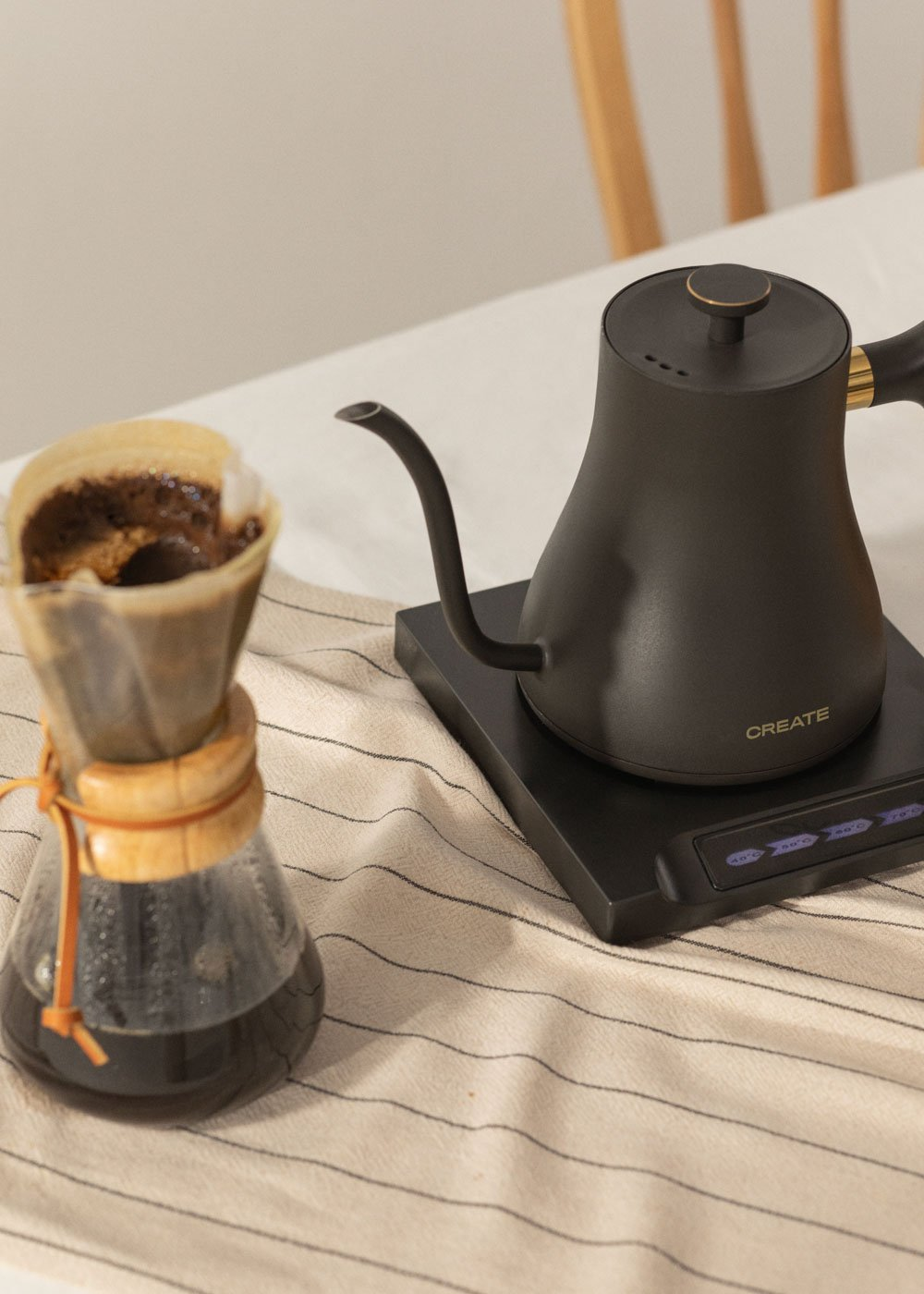 Una configuración de café con una tetera negra, un vertedor de vidrio y un paño a rayas sobre una mesa. Se está preparando café.