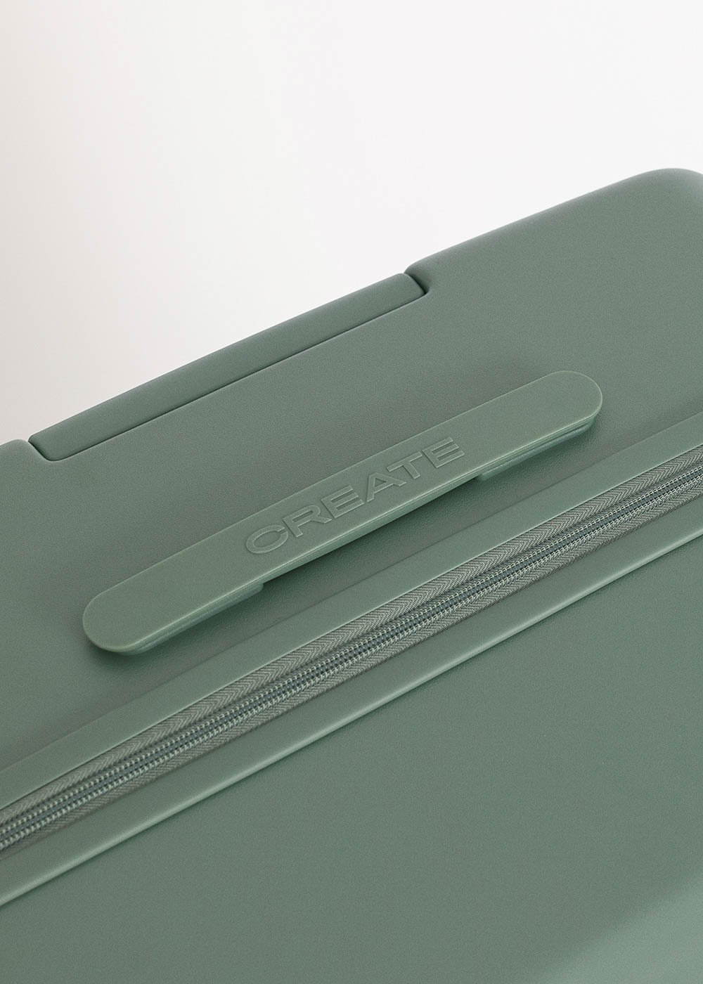 Primer plano de una maleta verde con la palabra 'CREATE' en el asa. Una cremallera recorre el borde de la maleta.