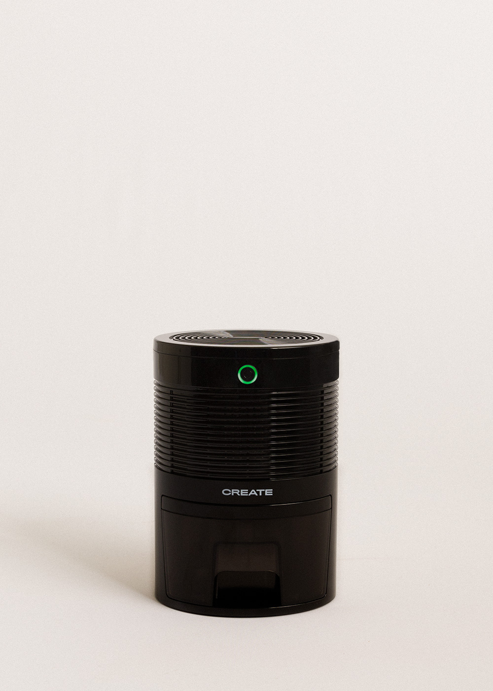 Purificador de aire negro con una luz verde en la parte superior, la palabra CREATE está impresa en el frente. Está sobre un fondo blanco.