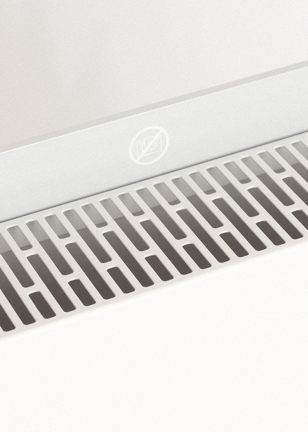 Primer plano de una rejilla de ventilación con patrón de rejilla. Arriba, una sección con un símbolo de prohibido fotografiar. Tonos blancos y grises.