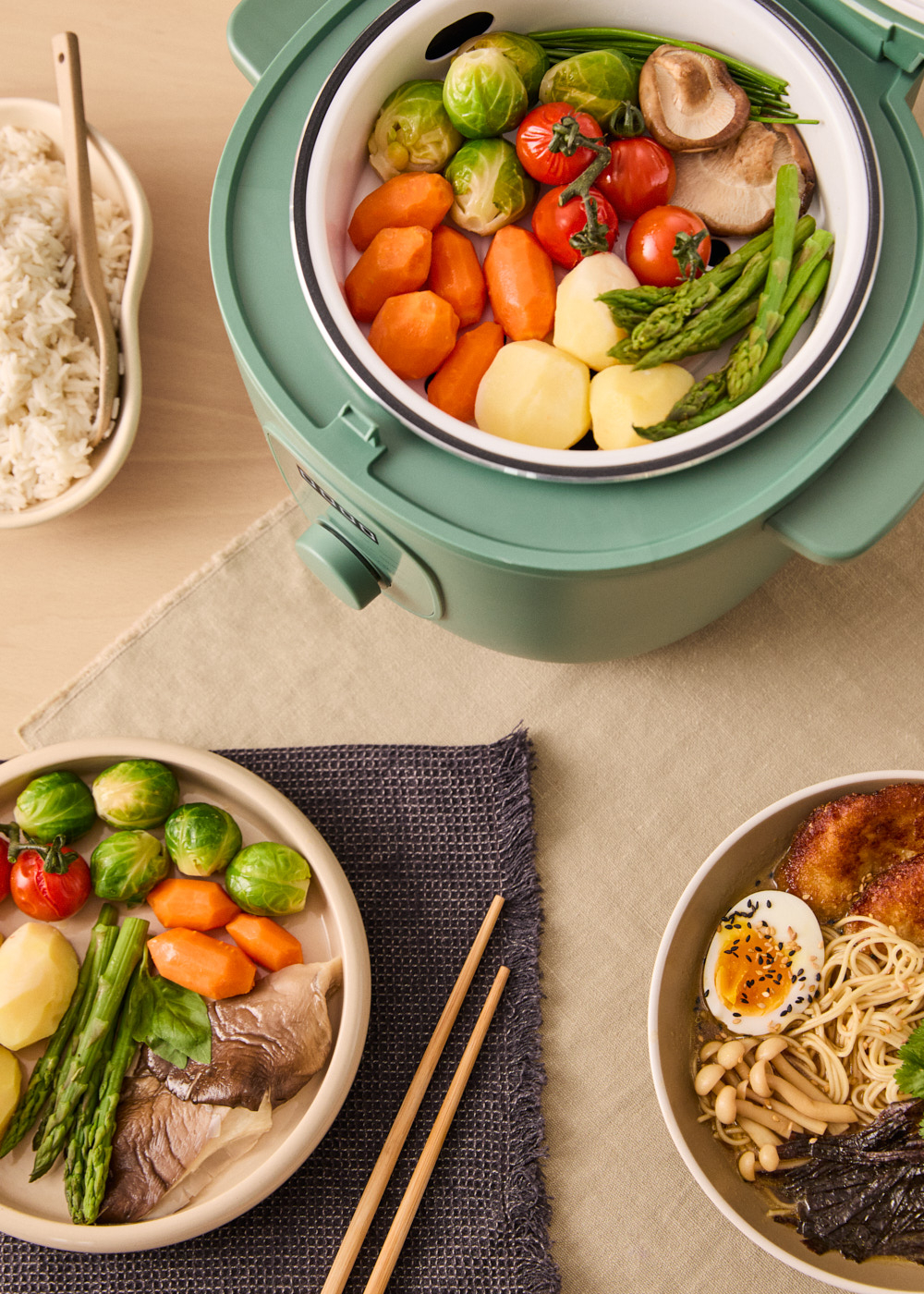 Una vaporera con verduras, un plato de verduras con palillos, un cuenco de arroz y ramen con huevo.