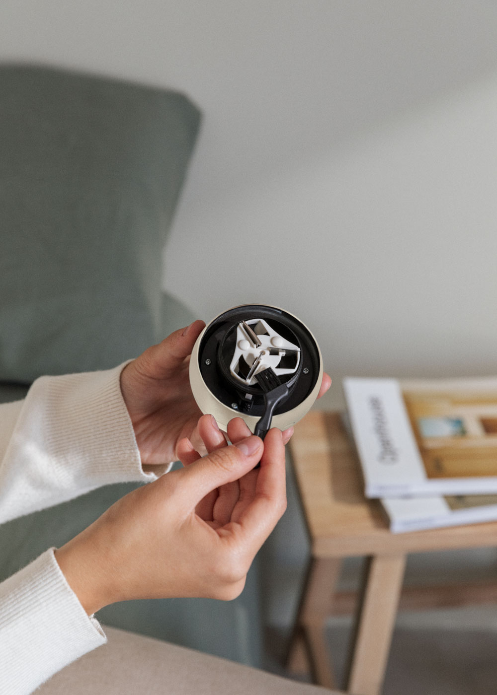 Una persona sostiene un dispositivo blanco y negro con un cepillo. Una mesa de madera y una revista están en el fondo.
