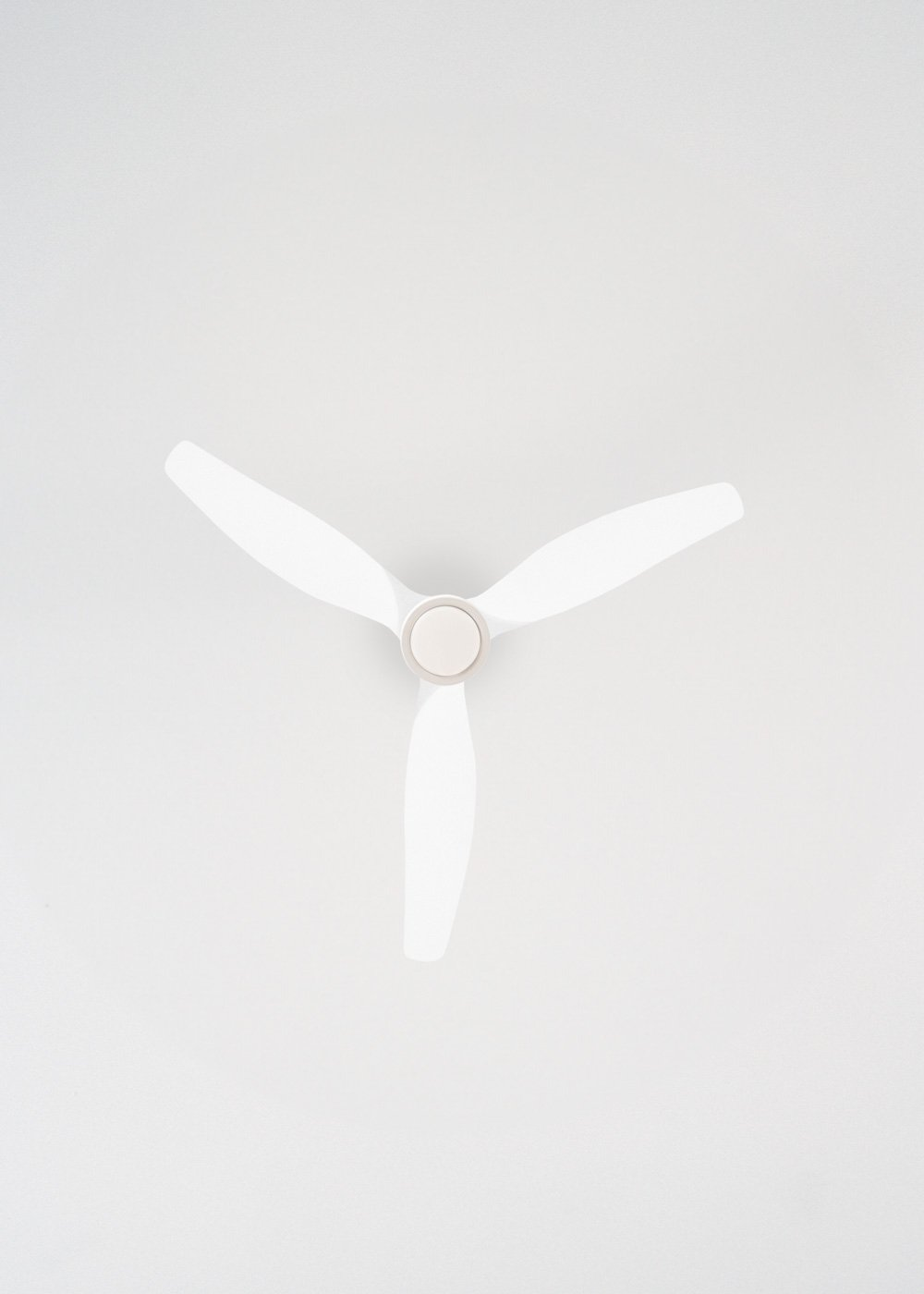 Un ventilador de techo blanco con tres aspas sobre un fondo blanco. El ventilador está centrado.