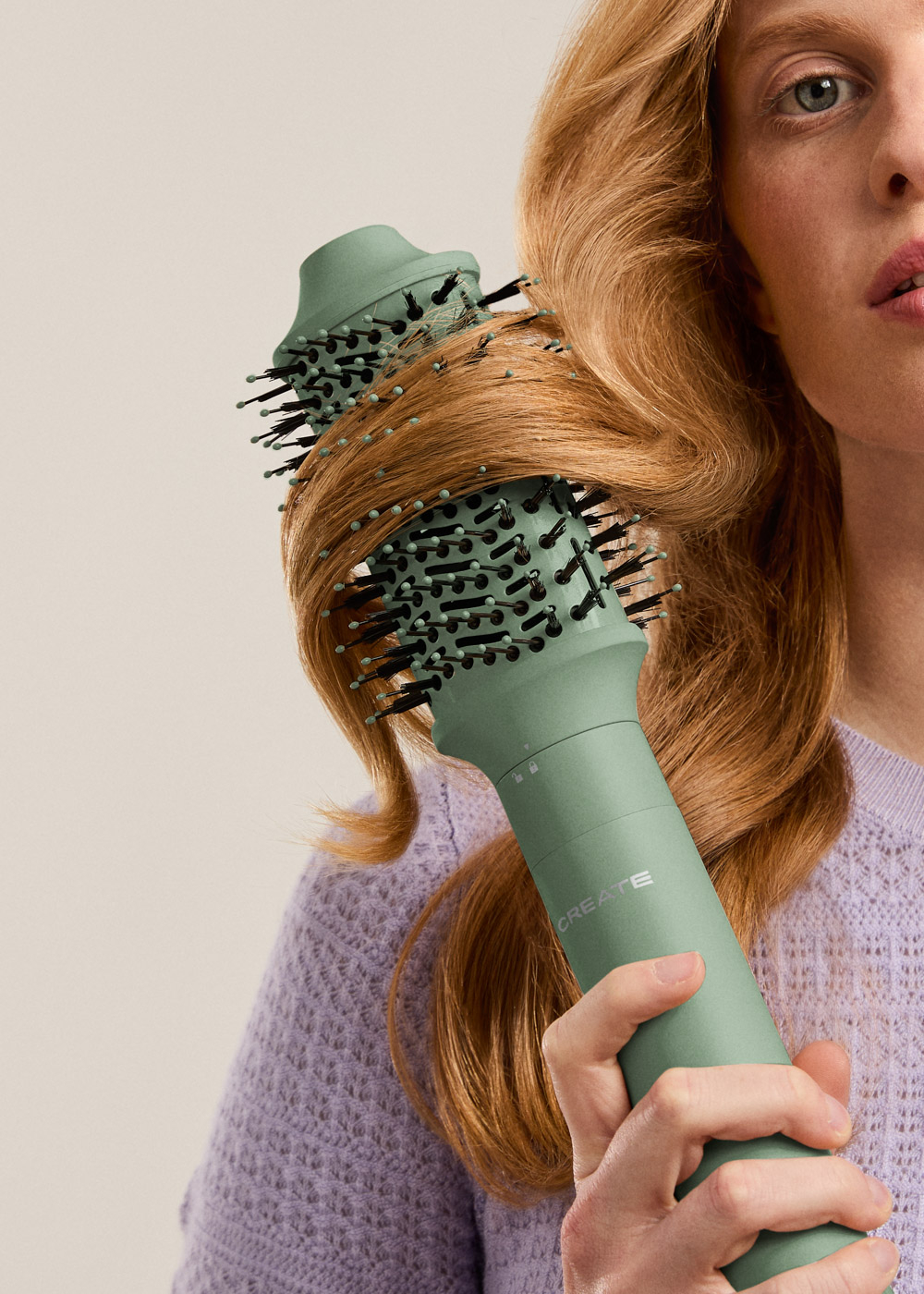 Una mujer sostiene un secador de pelo verde frente a su cabello castaño rojizo. El secador está peinado en el cabello.