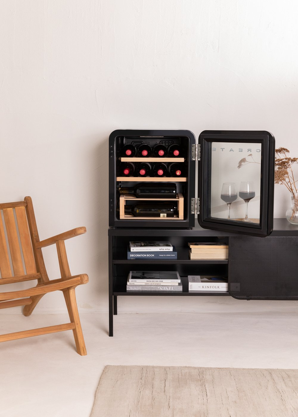 Una nevera de vino negra está abierta, mostrando botellas de vino. Una silla de madera está a la izquierda. Una alfombra y libros están en primer plano.