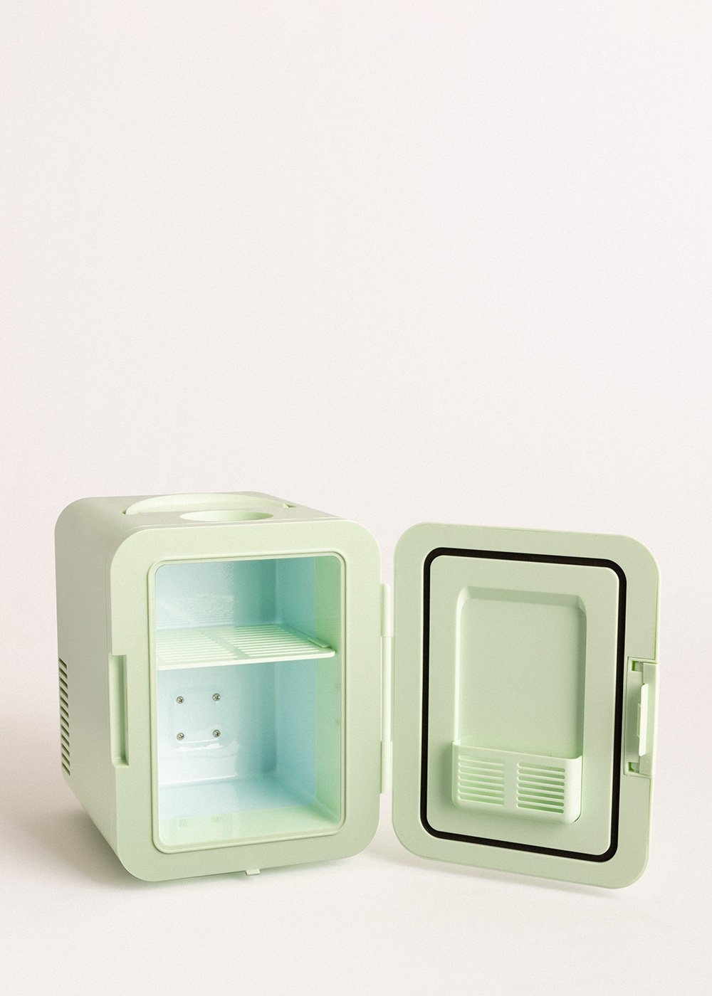 Un mini-frigorífico verde menta con la puerta abierta. El interior revela un estante. El fondo es blanco.