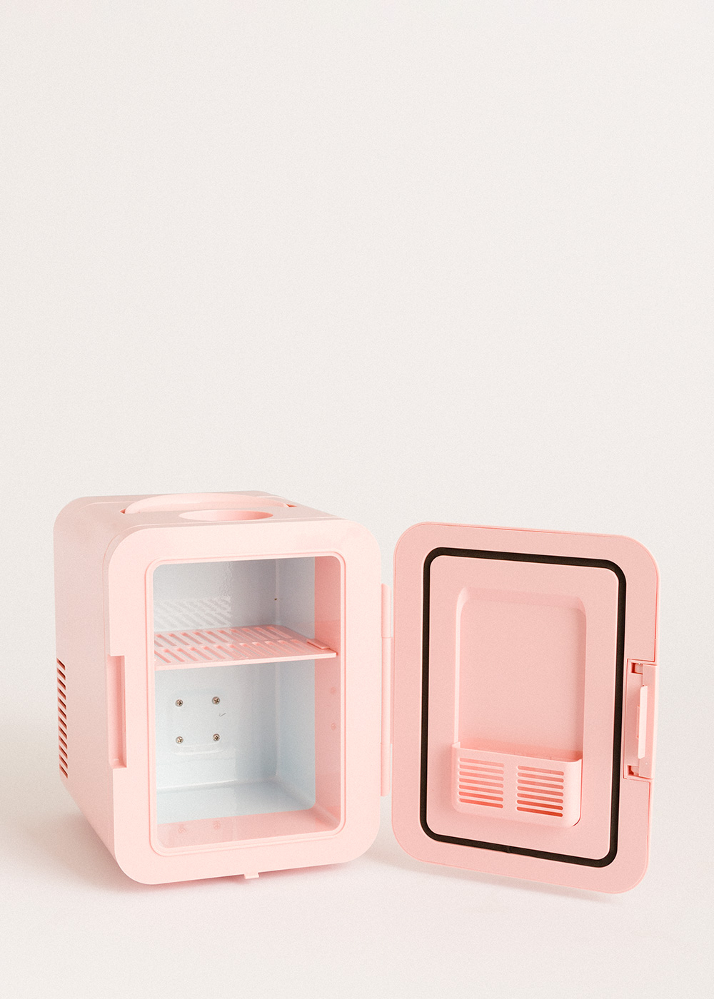 Una mini nevera rosa con la puerta abierta. El interior tiene un estante. El fondo es blanco.