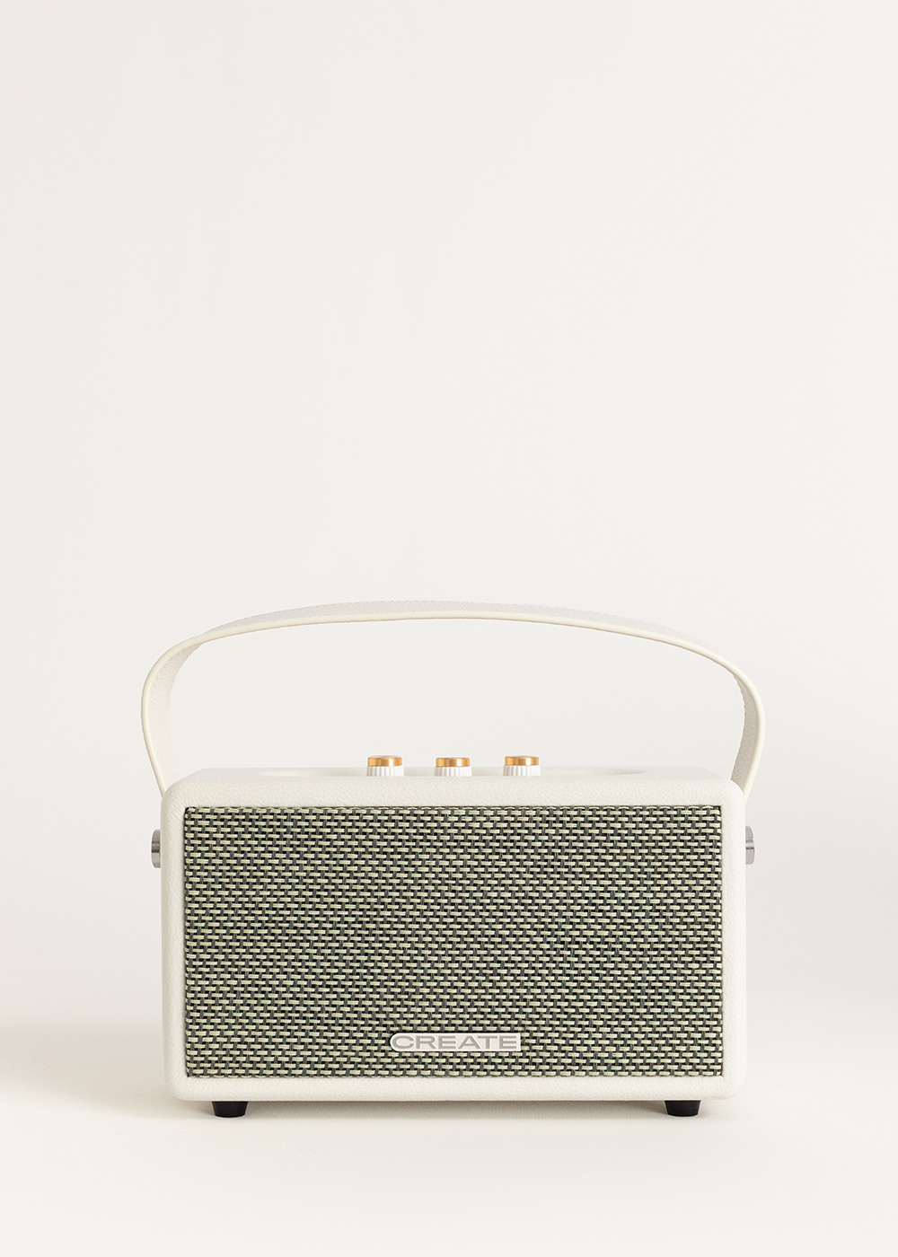 Un altavoz blanco y crema con asa. Tiene una parte frontal de malla, perillas doradas y la palabra "CREATE" en él.