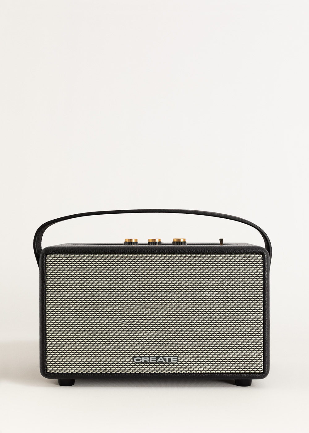 Altavoz blanco y negro con asa. El altavoz tiene una parte frontal tejida y perillas doradas en la parte superior. Fondo blanco.