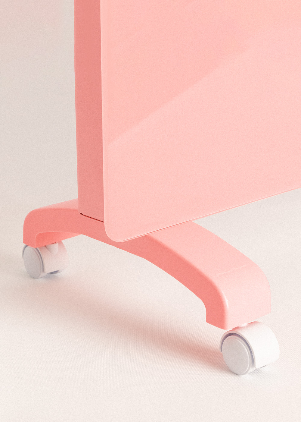 Primer plano de un escritorio rosa con una pata curva y ruedas sobre fondo blanco. El escritorio está a la izquierda.