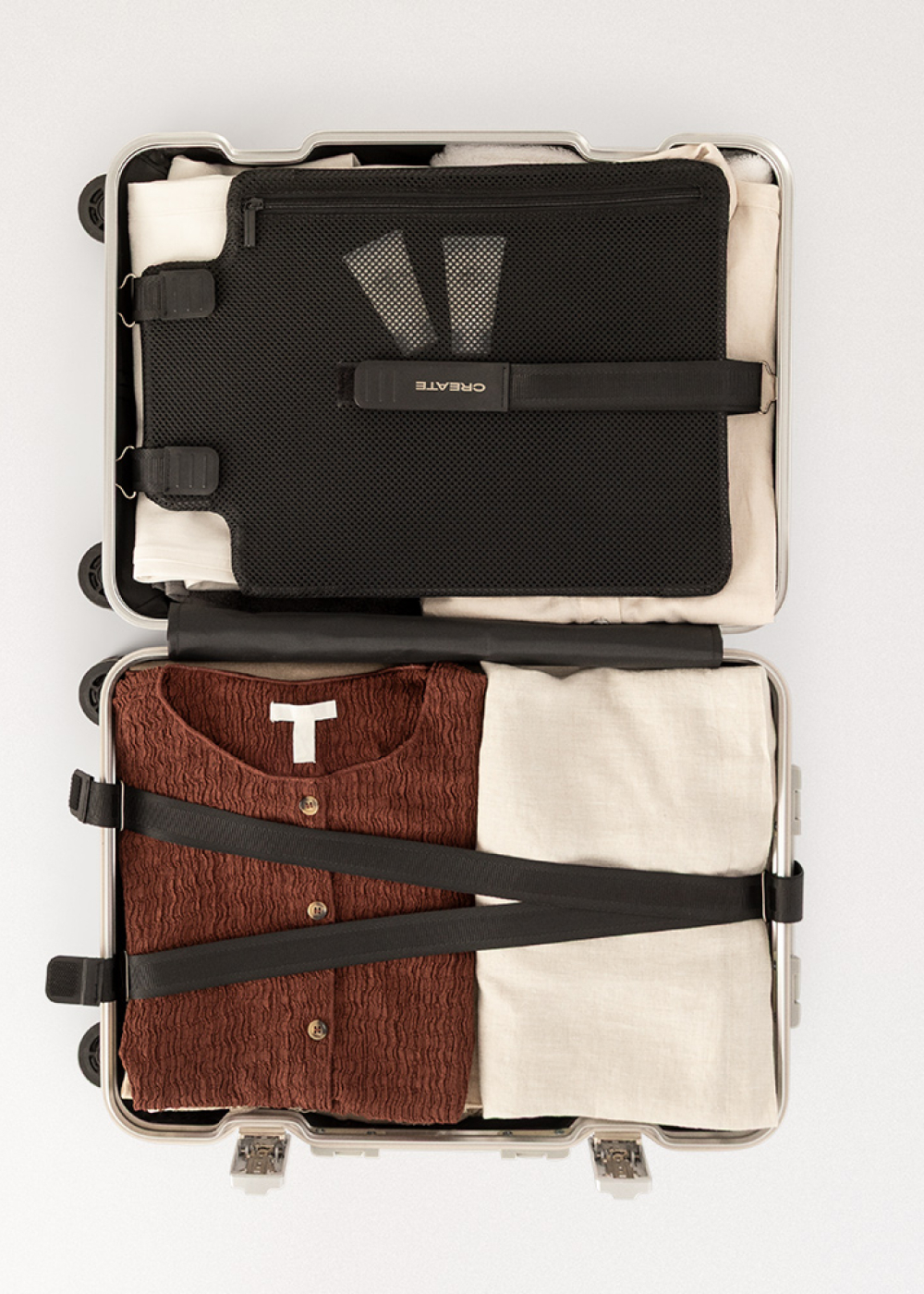 Maleta abierta con ropa, incluyendo una camisa marrón, pantalones crema y una bolsa de malla negra.