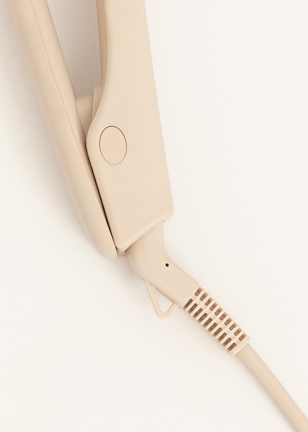 Una plancha de pelo beige sobre fondo blanco. El cable y el mango de la plancha son visibles.