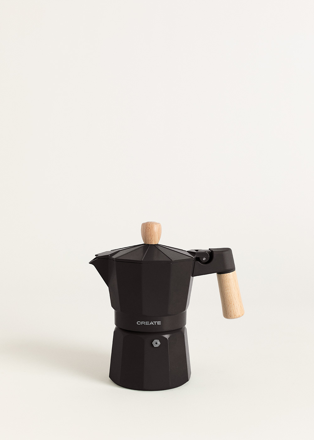 Una cafetera moka negra con mango y pomo de madera, sobre fondo blanco. La palabra "CREATE" está impresa en la cafetera.