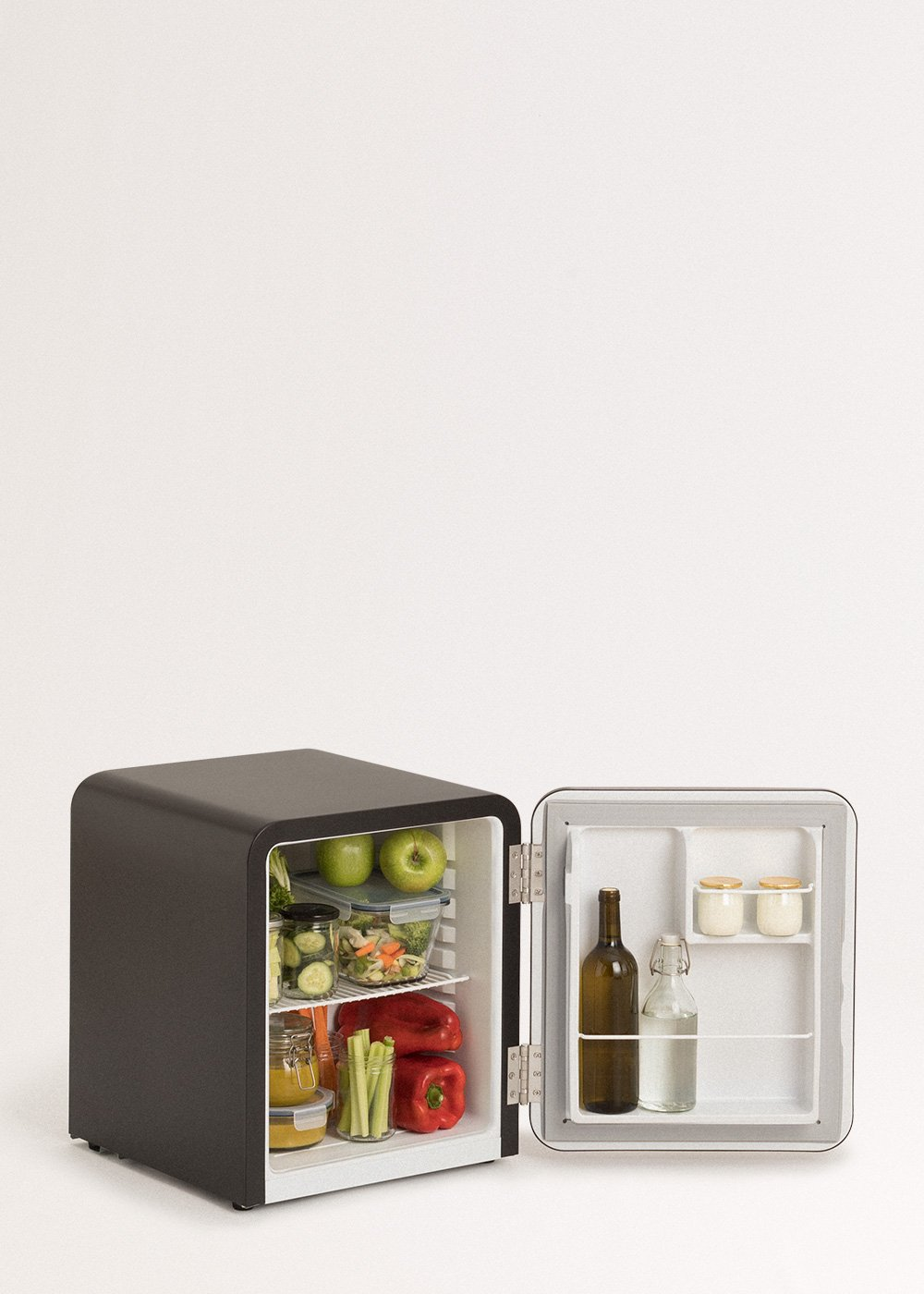 Un pequeño refrigerador negro con la puerta abierta. Dentro hay manzanas, verduras y botellas. El fondo es blanco.