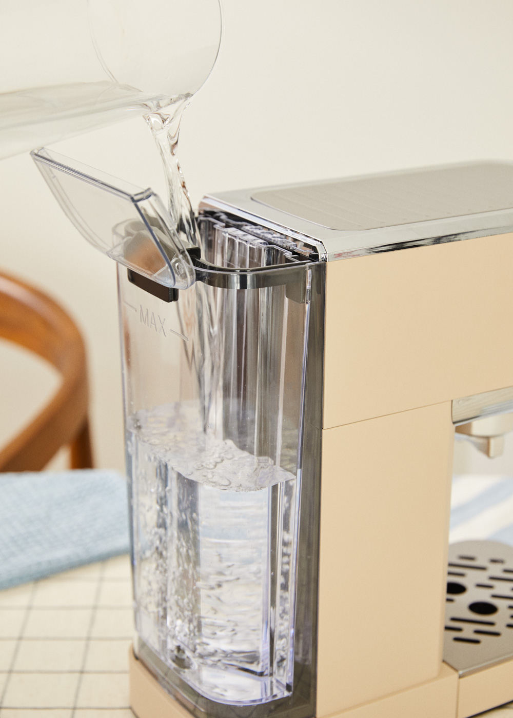 Agua vertiéndose en el depósito de agua de una cafetera. Máquina beige sobre una mesa. Se forman burbujas en el agua.