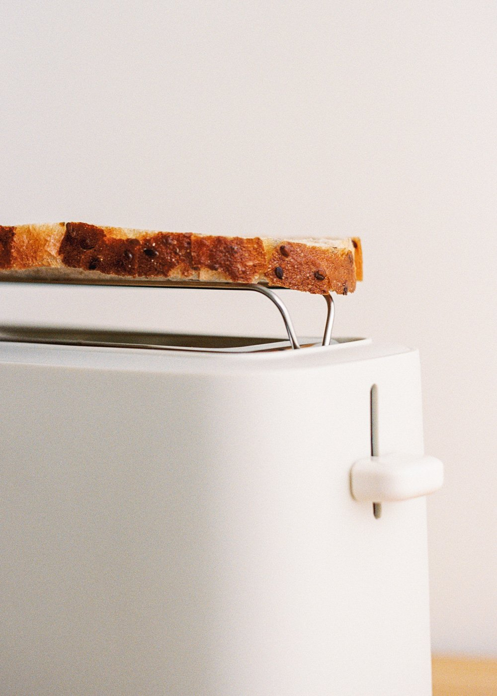 Una rebanada de pan tostado sobre una tostadora blanca. El pan es dorado con bordes oscuros, la tostadora es elegante.