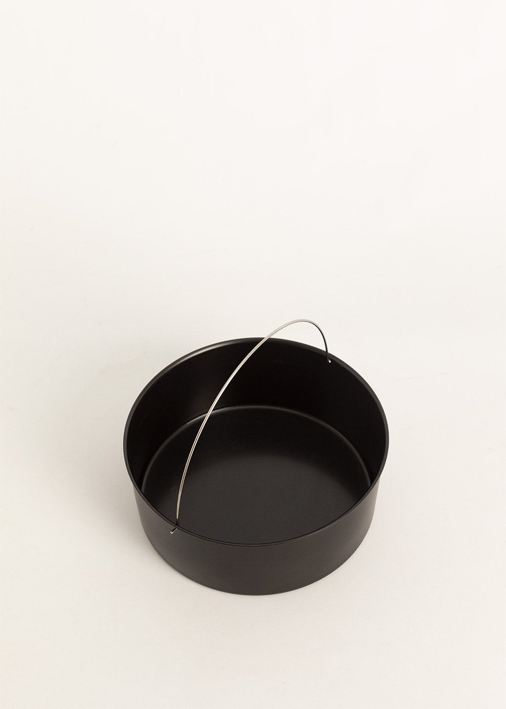 Un molde para hornear redondo negro con un asa plateada sobre un fondo blanco. La sartén está vacía.