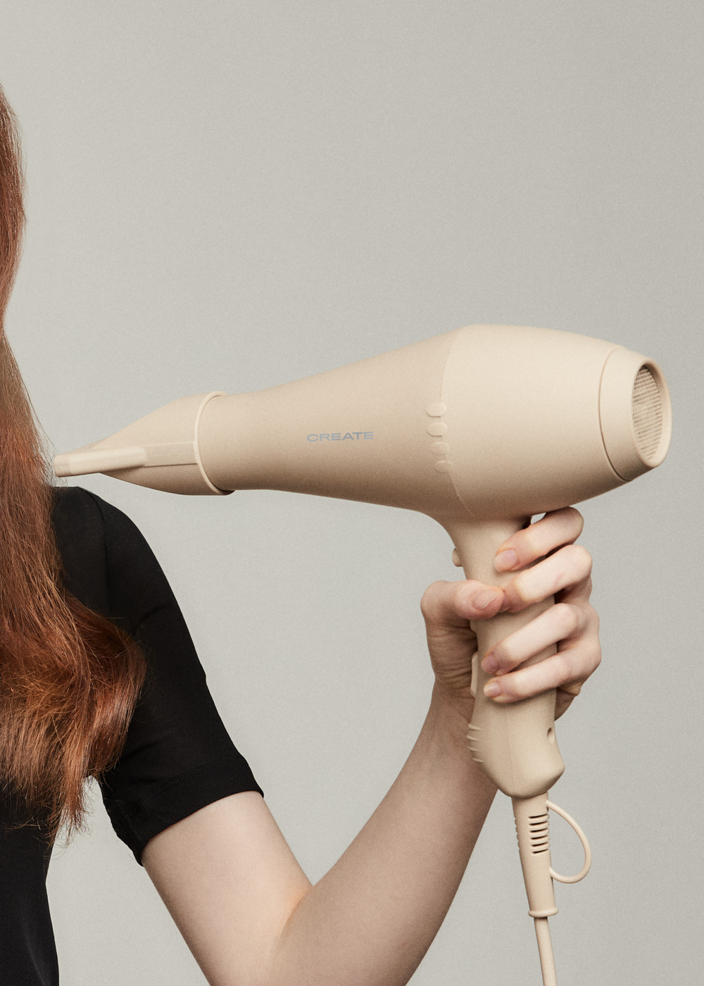 Una persona sostiene un secador de pelo beige con la palabra 'CREATE'. Cabello rojo y una camisa negra son parcialmente visibles.