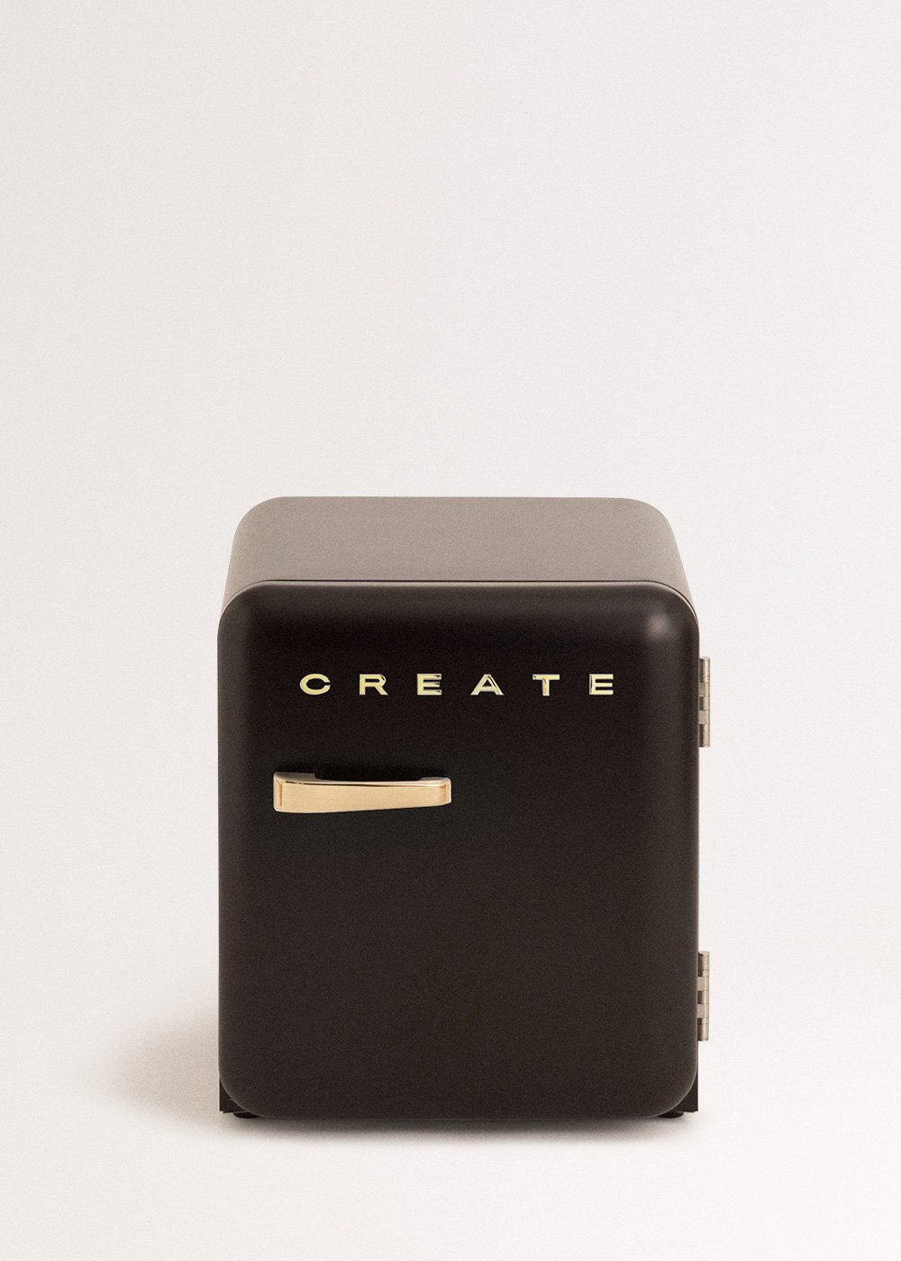 Un pequeño refrigerador negro con manija dorada y letras que dicen 'CREATE' al frente, sobre un fondo blanco.