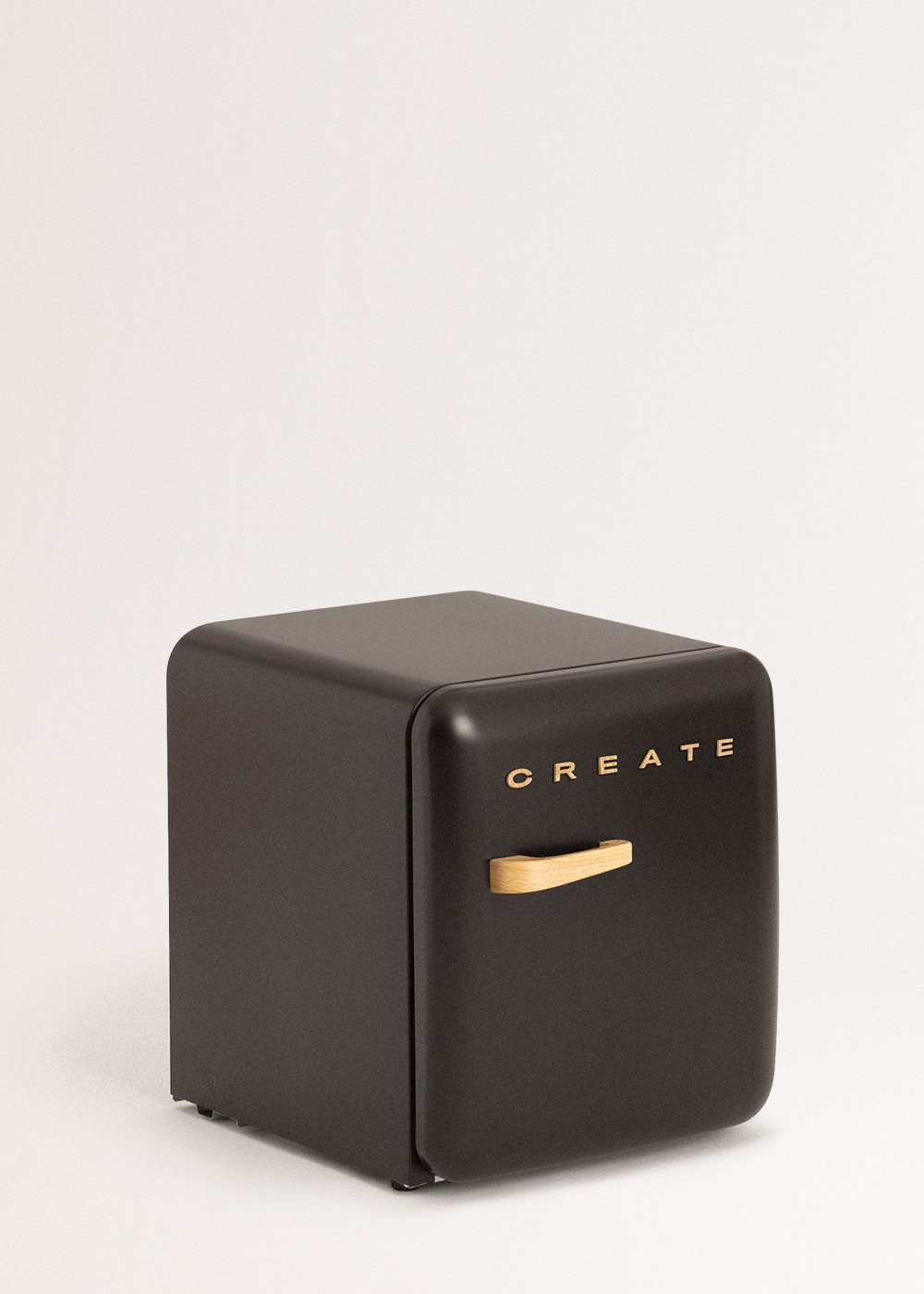 Un pequeño refrigerador negro con un asa de madera. La palabra 'CREATE' está impresa en dorado. Está sobre un fondo blanco.