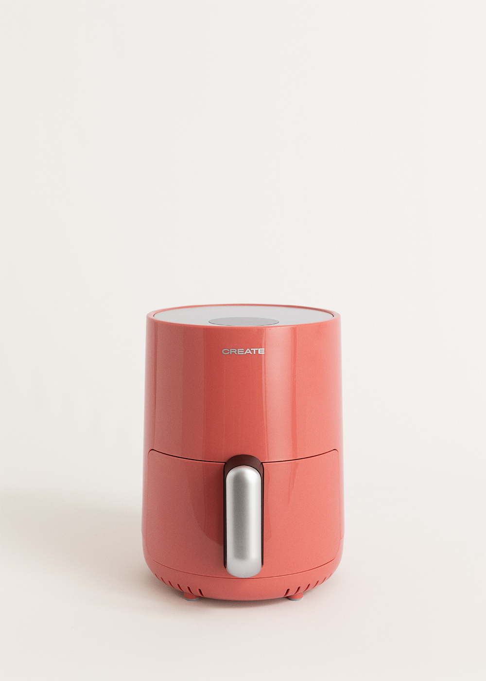 Una freidora de aire de color coral con asa plateada. El fondo es una superficie blanca lisa.