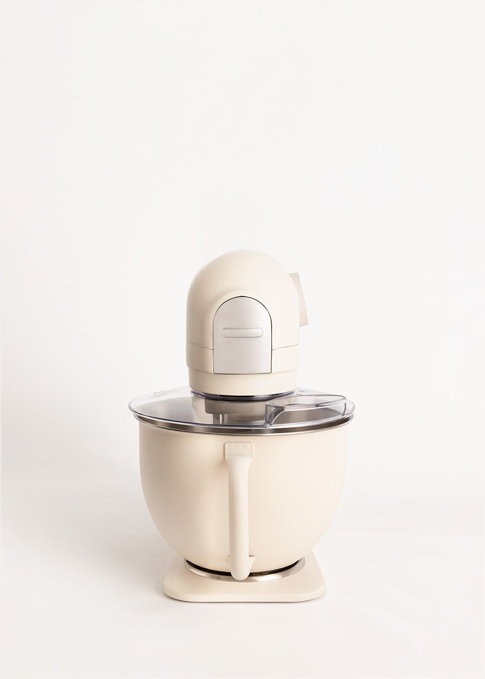 Una batidora de pie color crema sobre un fondo blanco. Tiene un cuenco, un asa y una parte superior con un motor plateado y crema.