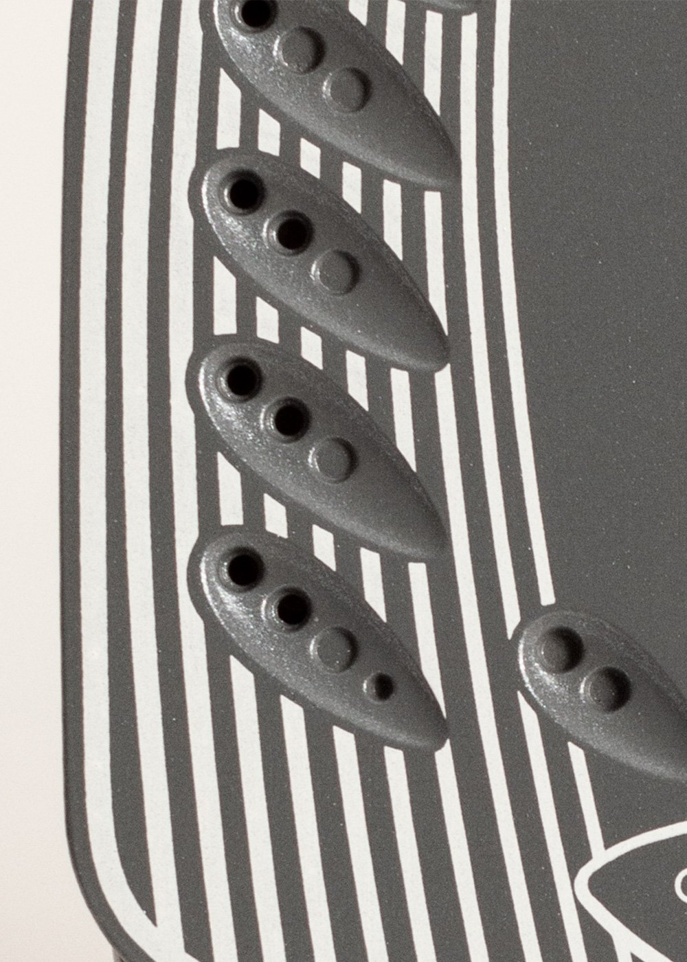 Primer plano de un diseño con elementos grises en forma de lágrima con agujeros y botones, sobre un fondo a rayas blanco y negro.