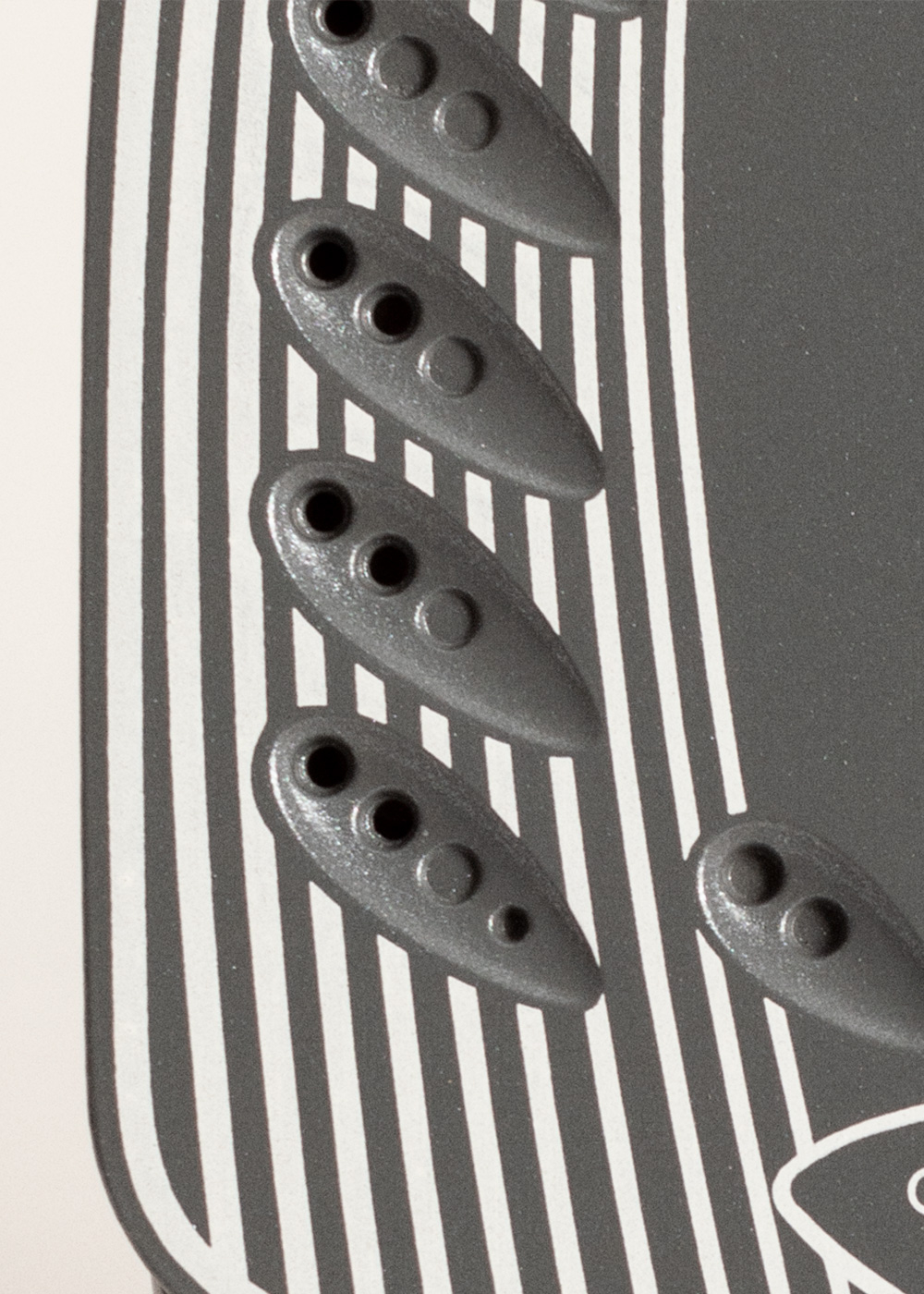 Primer plano de un diseño con elementos grises en forma de óvalo con círculos, sobre un fondo a rayas blanco y negro.