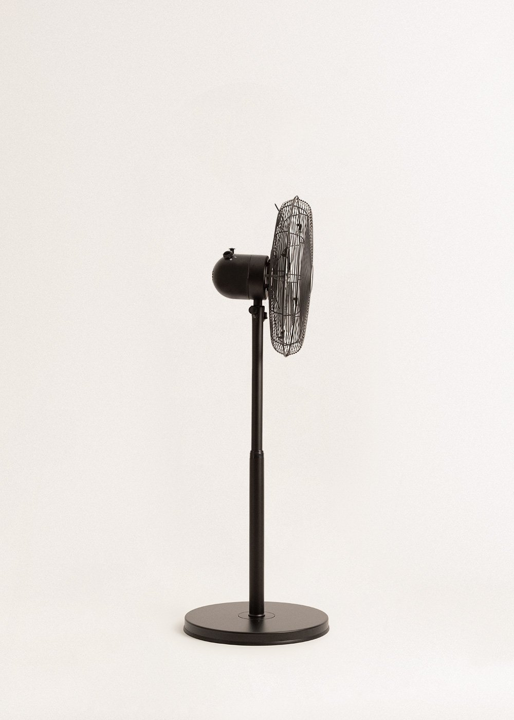 Un ventilador negro de pie sobre un fondo blanco. El ventilador está girado hacia un lado.