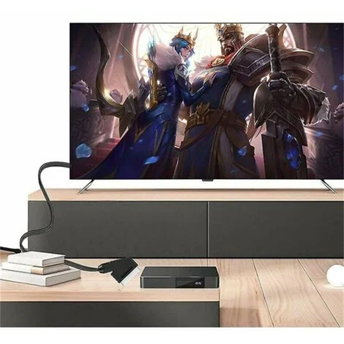 Der Fernseher zeigt eine Fantasieszene. Darunter eine schwarze Box, Kabel und Bücher auf einem hellen Holztisch.
