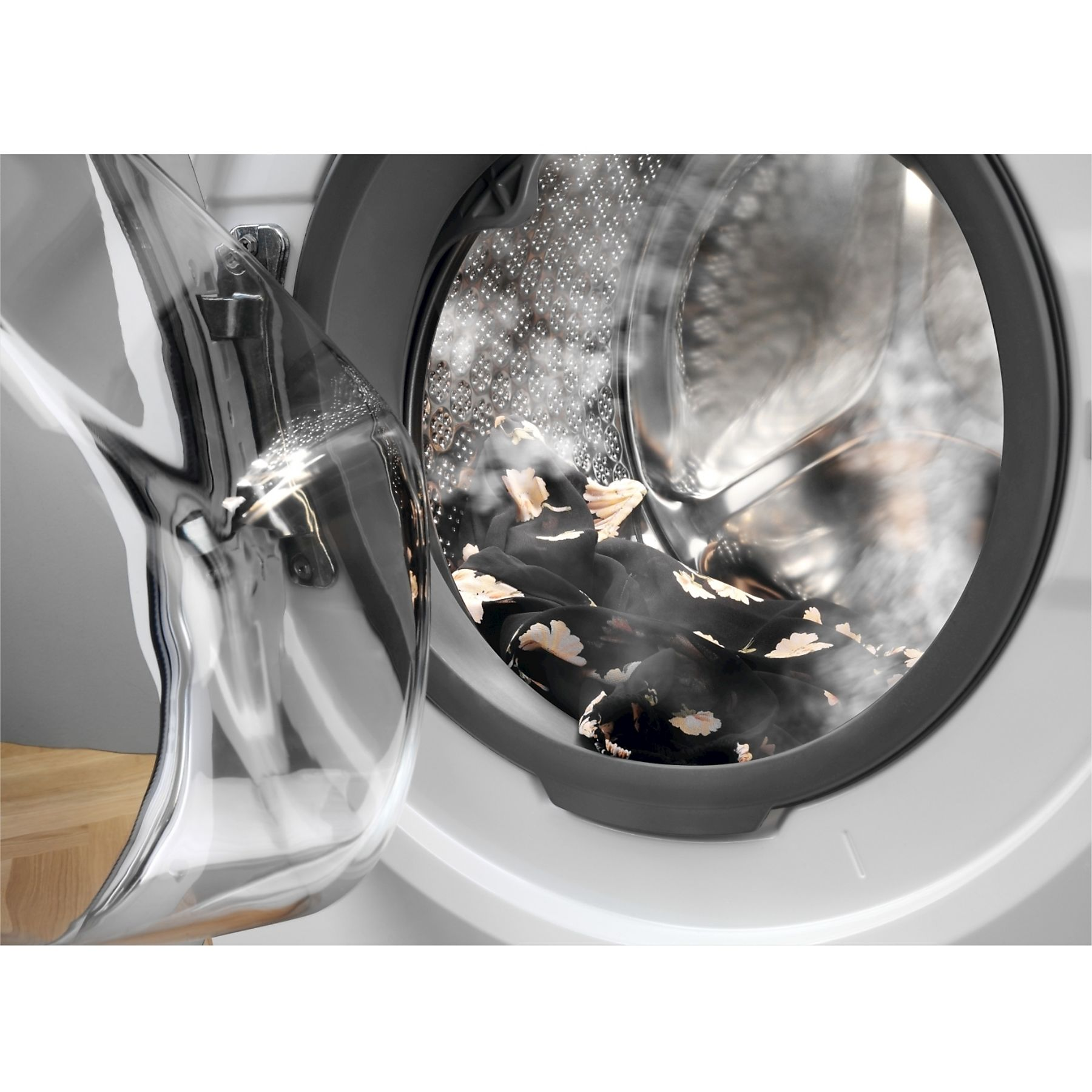 Lavatrice aperta con vestiti floreali neri all'interno. Vapore visibile. Porta in vetro trasparente aperta, luce riflessa.