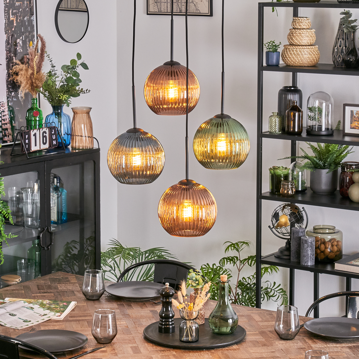 Esszimmer mit Holztisch, vier Hängelampen und einem schwarzen Regal mit Pflanzen und Dekorationen.
