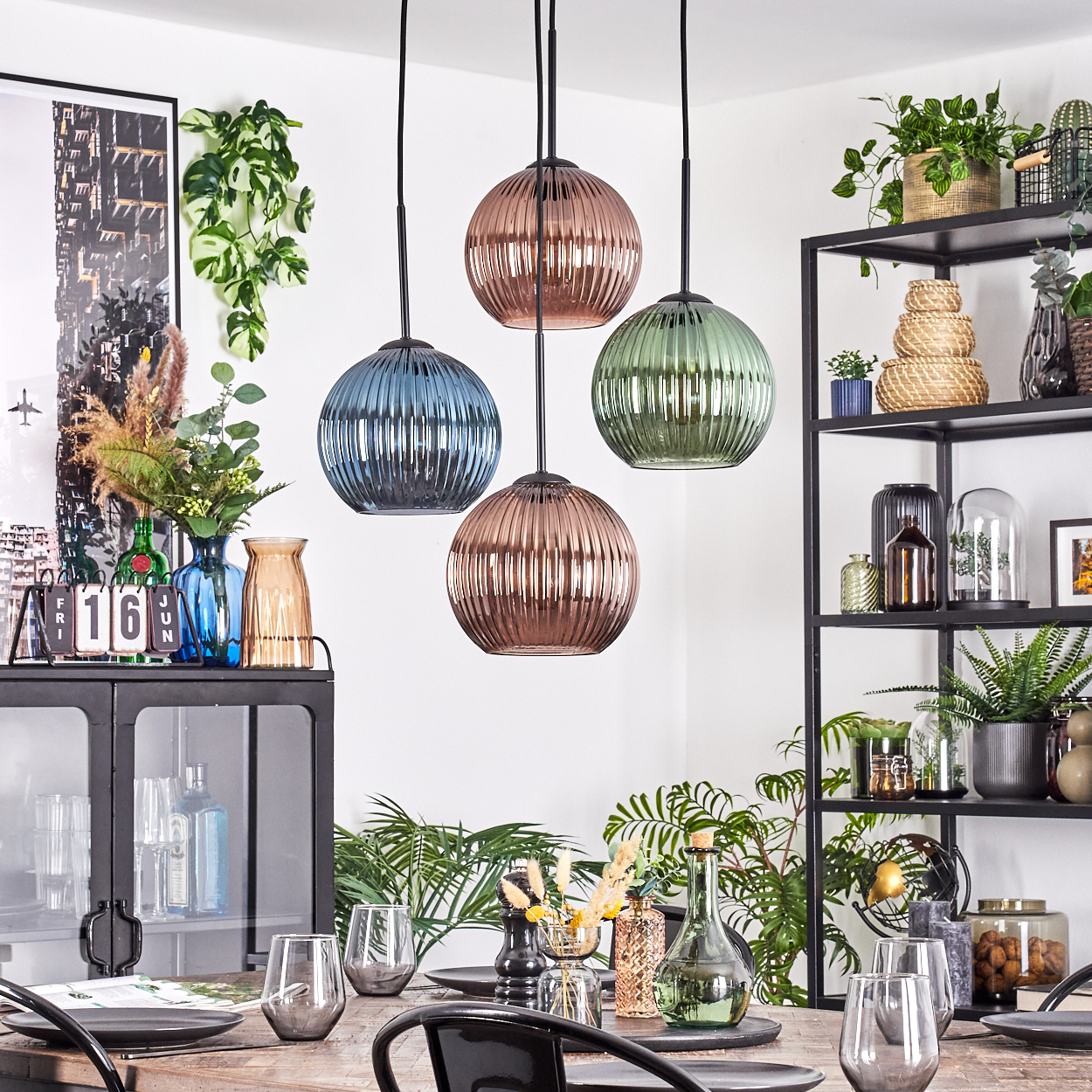 Esszimmer mit vier bunten Pendelleuchten, Tisch mit Gläsern und Tellern, Pflanzen und Dekorationsartikeln.