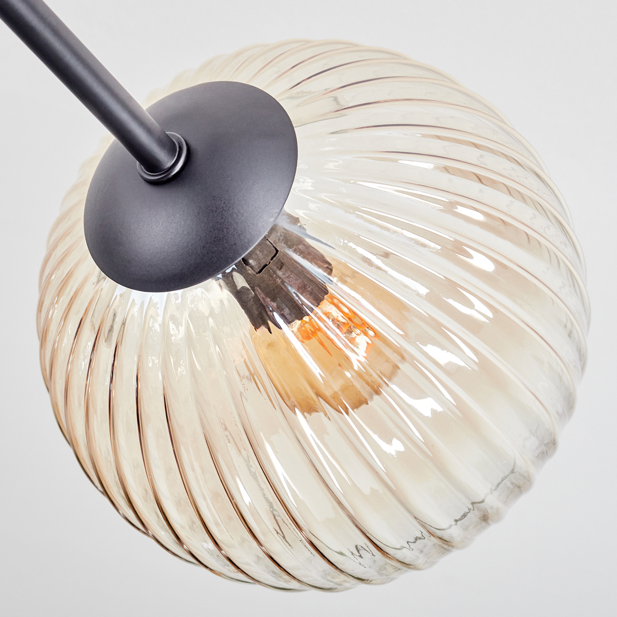 Nahaufnahme einer Leuchte. Sie hat einen runden, gerippten Glasschirm in Creme und eine schwarze Metallhalterung.
