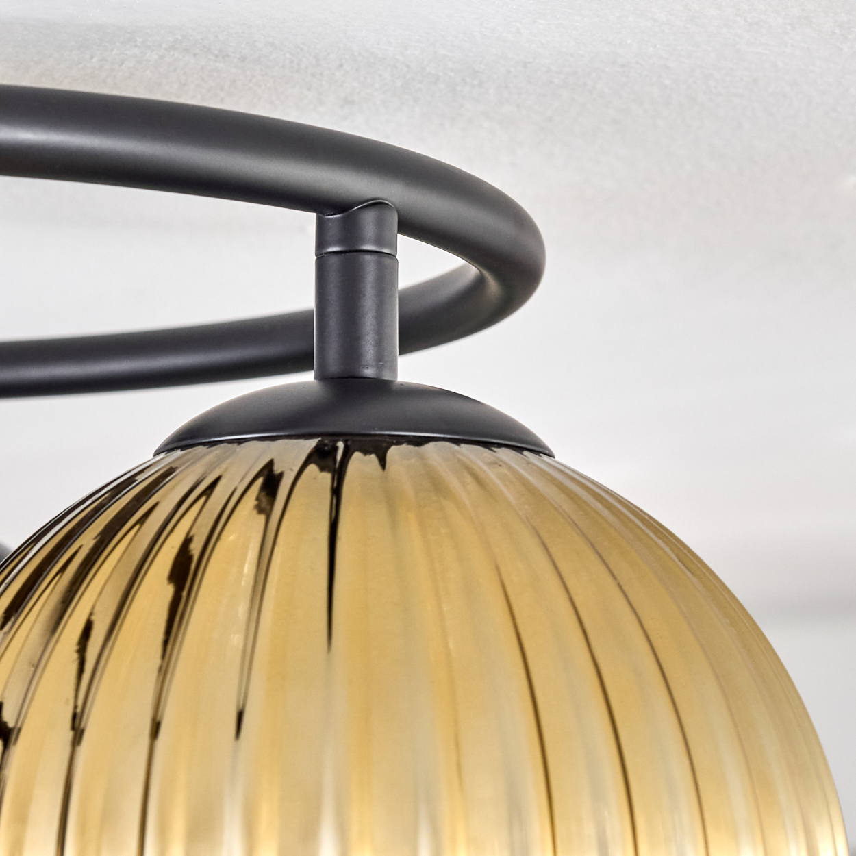 Nahaufnahme einer Deckenlampe. Sie hat einen schwarzen Metallrahmen und einen gelben Glasschirm. Der Hintergrund ist weiß.