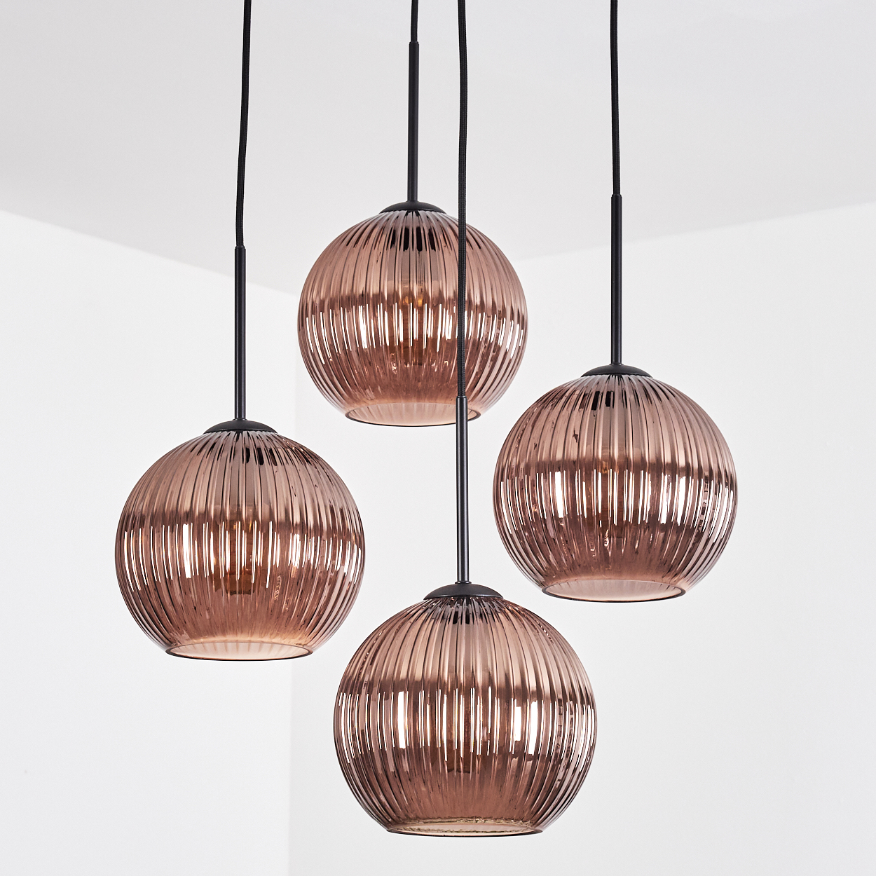 Vier kupferfarbene Pendelleuchten hängen an schwarzen Kabeln und Stielen. Jede hat einen gerippten, kugelförmigen Glasschirm.