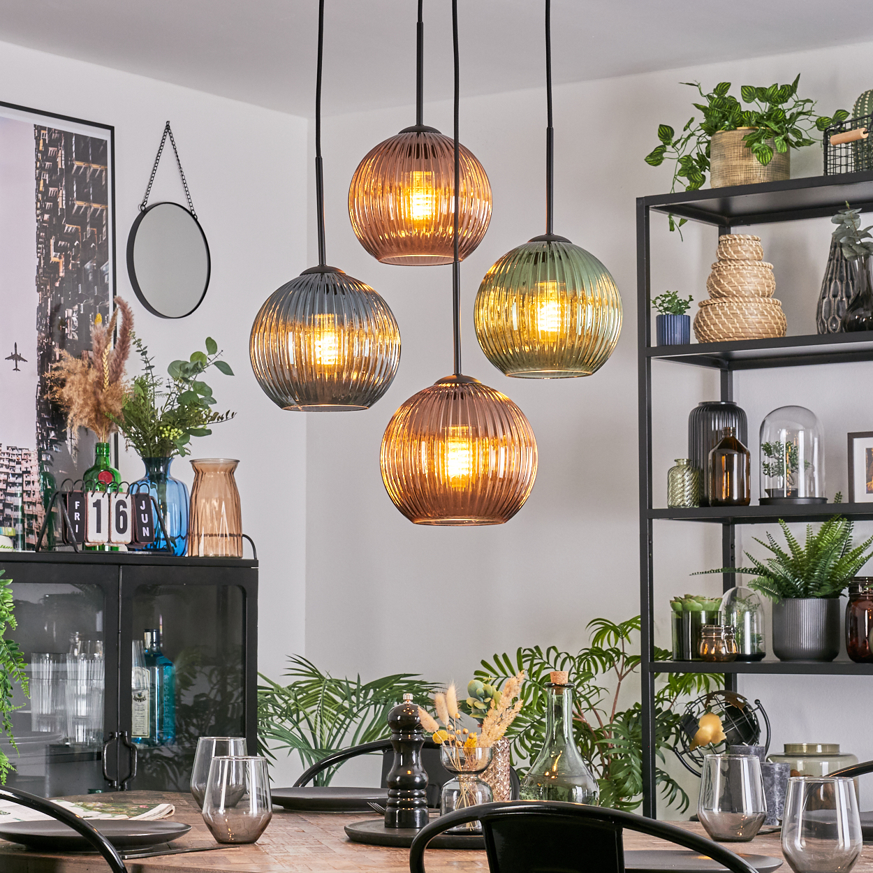 Esszimmer mit vier Kugellampen. Pflanzen, Gläser und eine Tischdekoration sind sichtbar. Rechts ist ein schwarzes Metallregal.