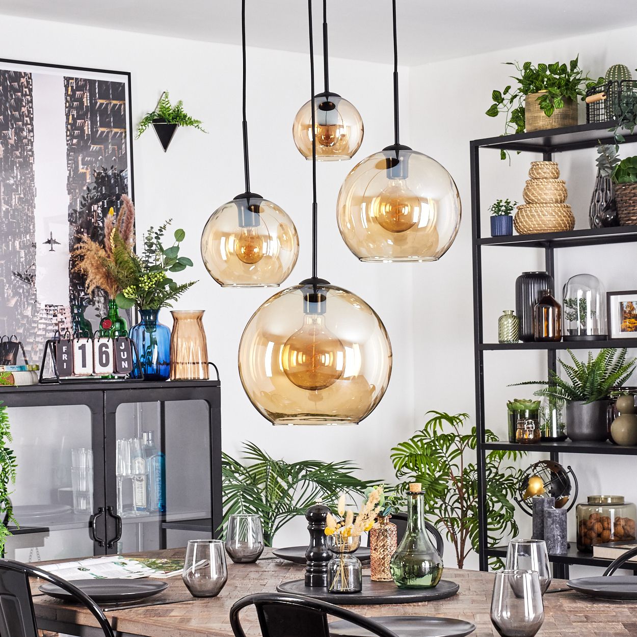 Esszimmer mit hängenden Kugelleuchten, Tisch, Stühlen, Pflanzen und Dekorationsartikeln. Ein schwarzes Metallregal im Hintergrund.