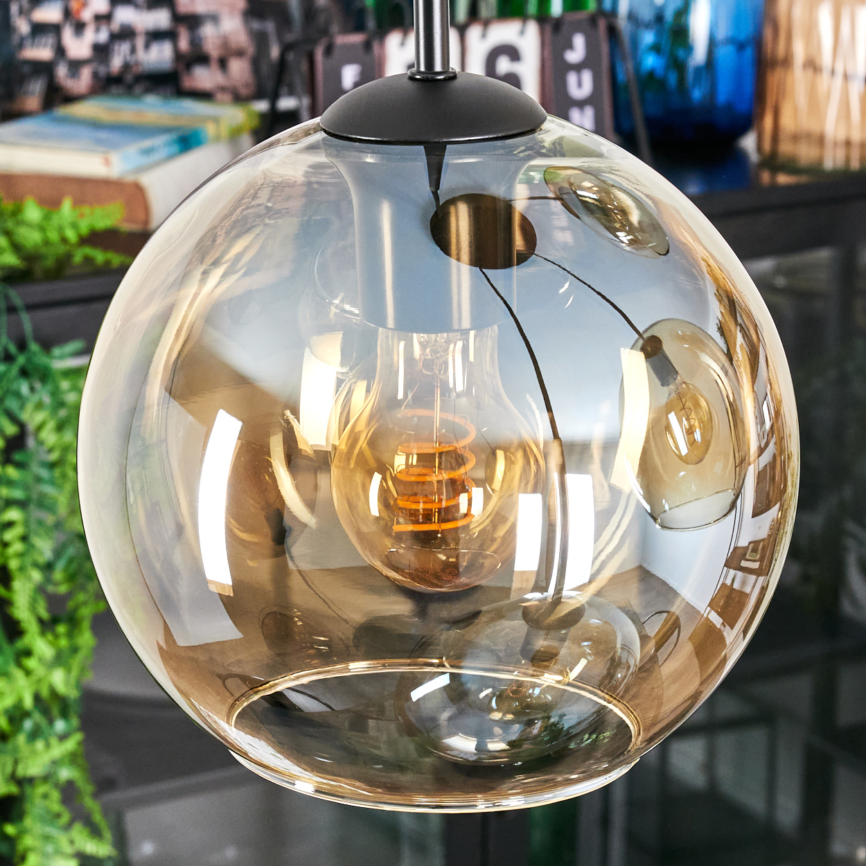 Nahaufnahme einer kugelförmigen Glaslampe mit sichtbarer Glühbirne. Die Lampe ist von oben aufgehängt. Der Hintergrund ist unscharf.