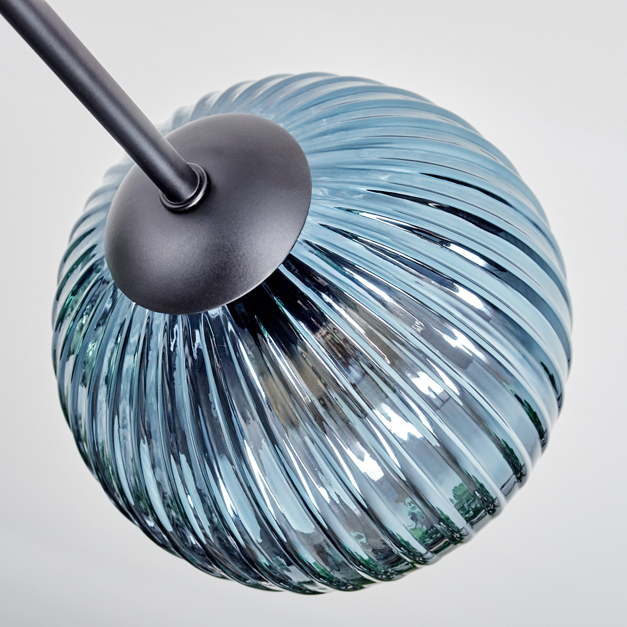 Nahaufnahme eines blauen Glaslampenschirms mit schwarzem Metallarm und Halterung. Der Schirm hat vertikale Rillen.