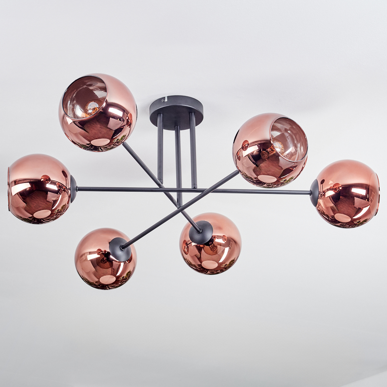 Eine moderne Deckenleuchte mit sechs kupferfarbenen Kugelschirmen. Dunkelgraue Metallarme erstrecken sich von einer zentralen Halterung.