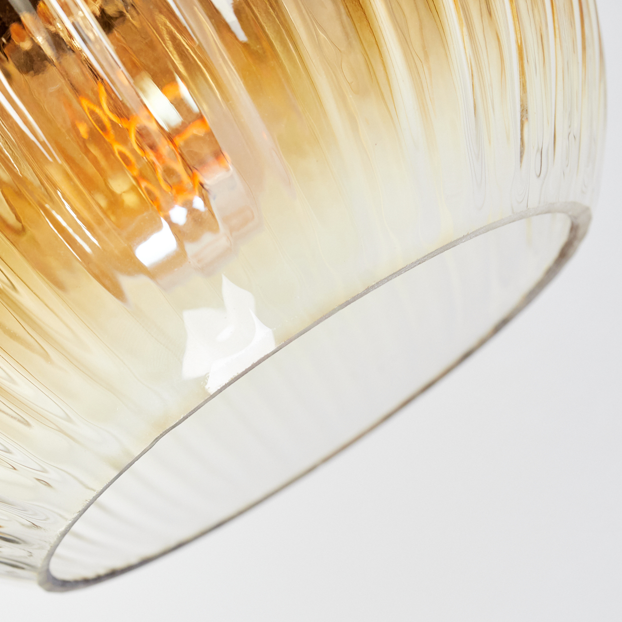 Nahaufnahme eines Glasschirms. Er ist bernsteinfarben mit vertikalen Rippen. Der Hintergrund ist weiß, und die Glühbirne ist sichtbar.