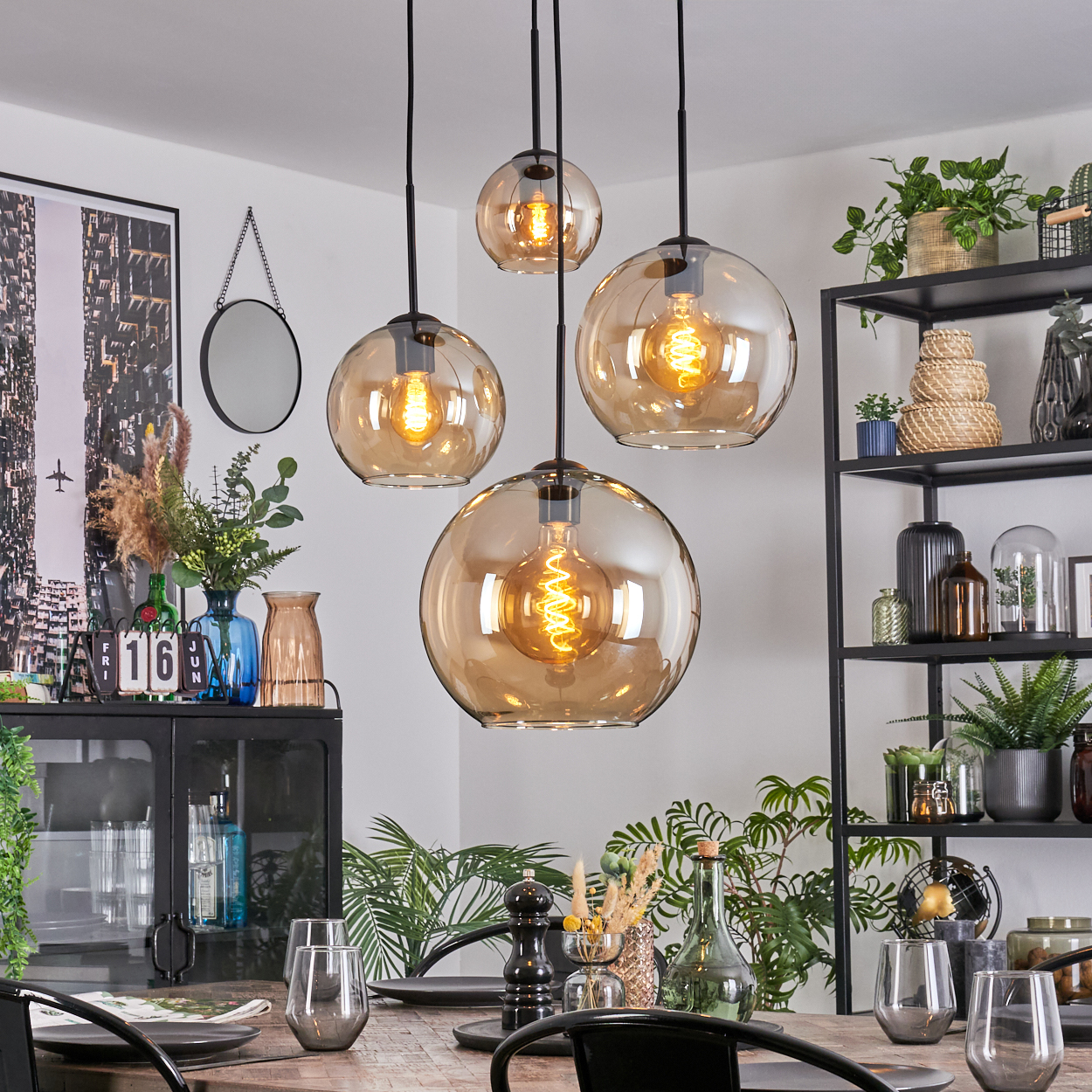 Esszimmer mit vier kugelförmigen Pendelleuchten. Pflanzen, Gläser und ein Tisch im Vordergrund, Regale im Hintergrund.