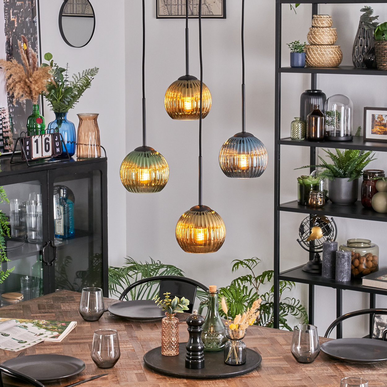 Ein Esszimmer mit einem Holztisch, der für eine Mahlzeit gedeckt ist. Vier Pendelleuchten hängen darüber. Auf der rechten Seite sind Regale.