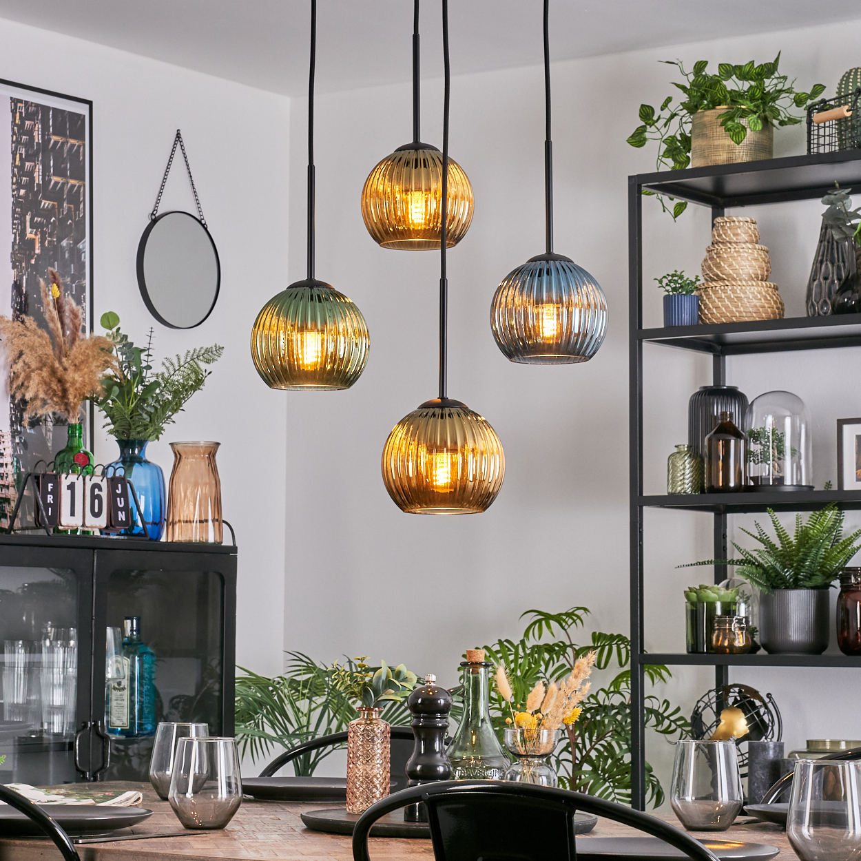 Esszimmer mit Hängekugelleuchten, gedecktem Tisch, Pflanzen und schwarzem Regal. Neutrale Töne und warme Beleuchtung.