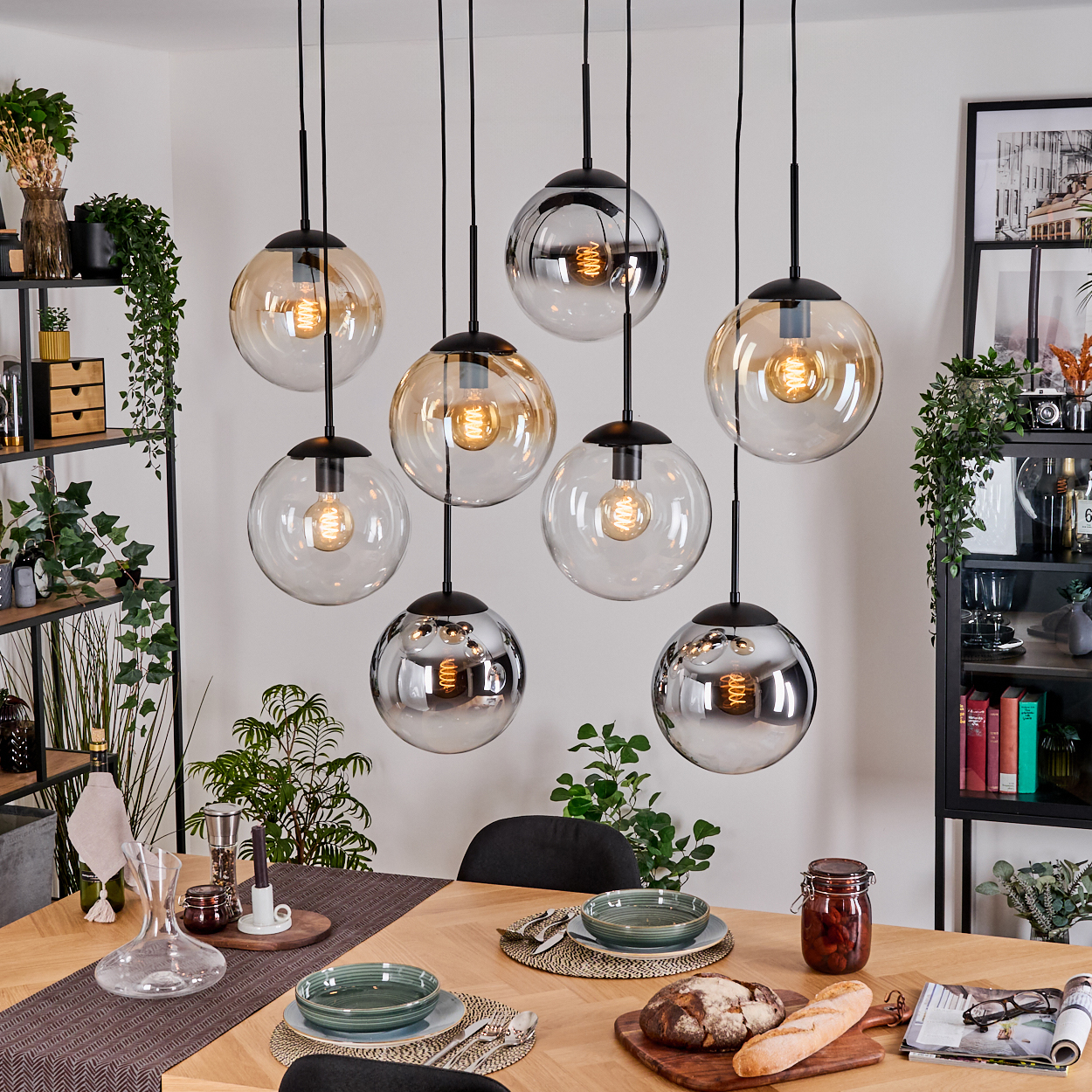 Esszimmer mit acht kugelförmigen Pendelleuchten. Tisch mit Tellern, Brot und Glas. Regale mit Pflanzen und Dekor.
