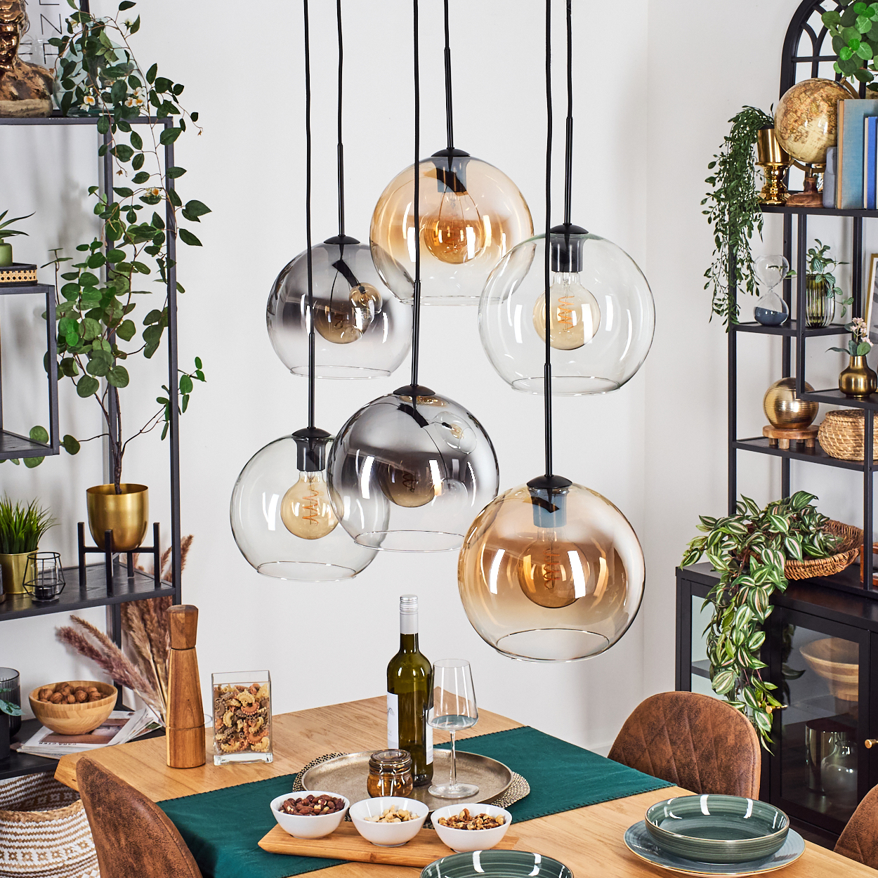 Esszimmer mit Pendelleuchten. Tisch mit Essen, Wein und Tellern. Regale mit Pflanzen und Deko im Hintergrund.