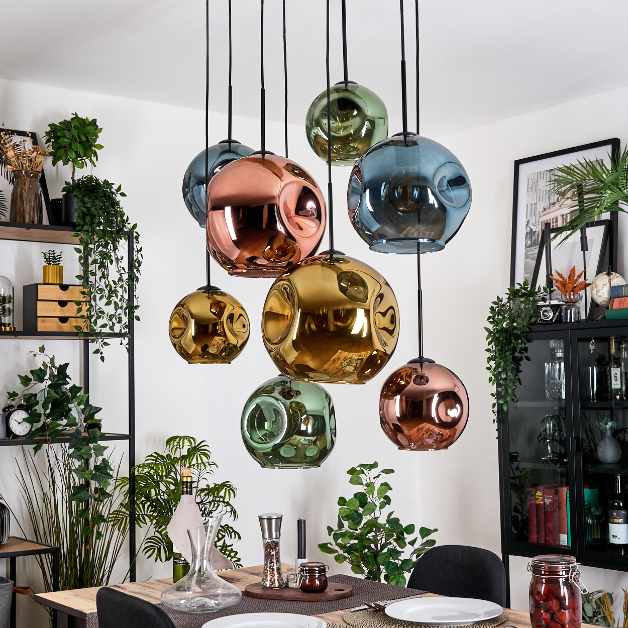 Esszimmer mit Tisch, hängenden Kugelleuchten in verschiedenen Farben, Regalen mit Pflanzen und Deko, und einem schwarzen Schrank.