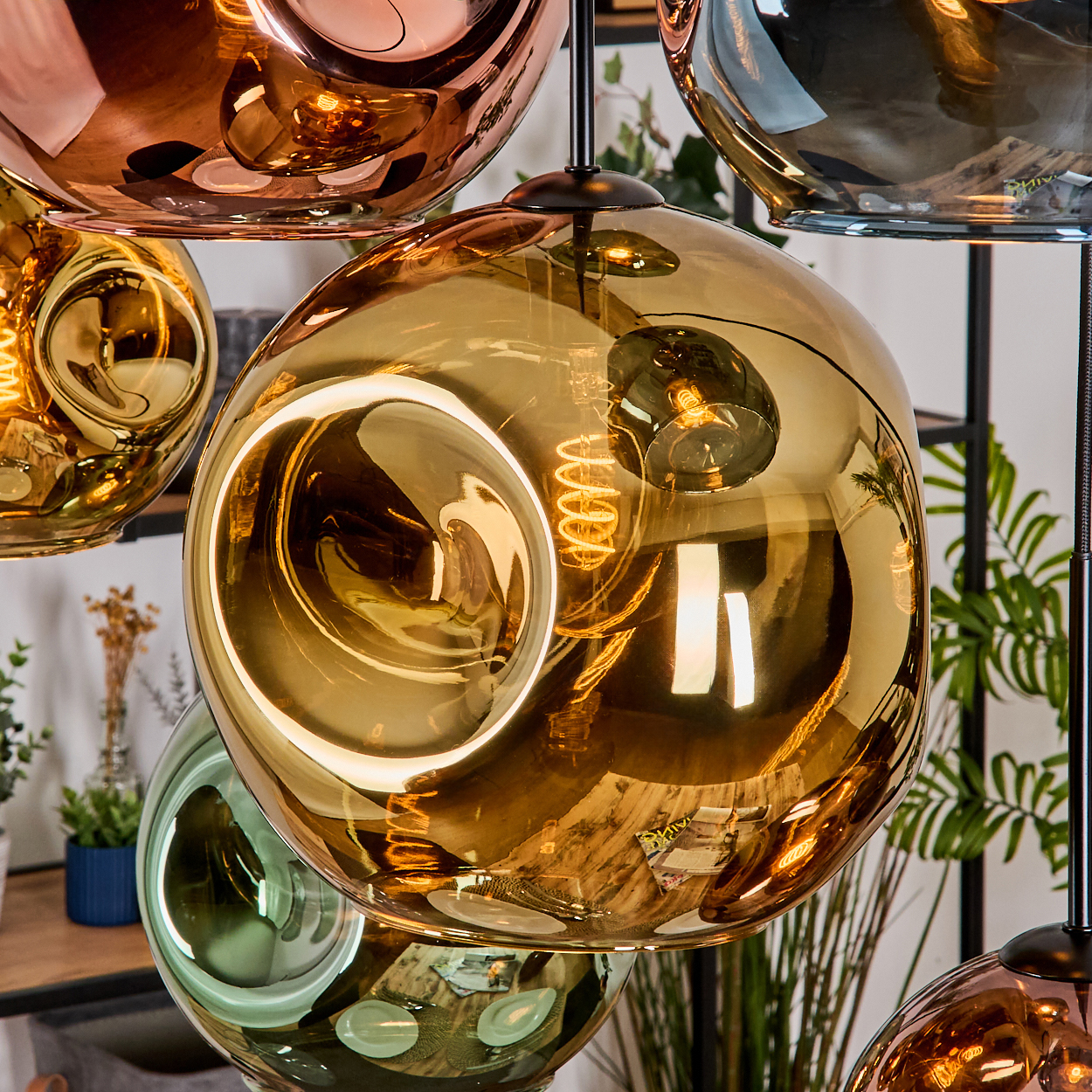 Nahaufnahme von modernen Pendelleuchten mit metallischen, gläsernen Kugeln. Einige sind kupferfarben, goldfarben und grün. Sichtbare Wendelglühbirnen im Inneren der Kugeln.