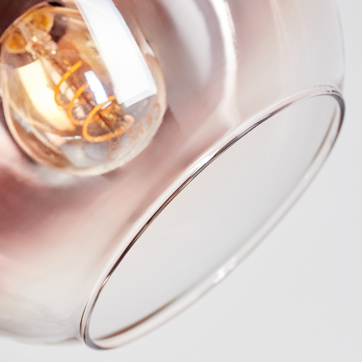 Nahaufnahme einer Glasleuchte mit sichtbarer Glühbirne. Das Glas hat einen rosafarbenen Farbton. Der Hintergrund ist weiß.